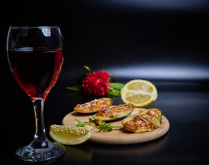mussels baked delicacy on a round wooden plate with a slice of lemon on a dark background