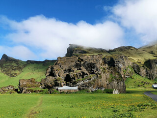 Idyllic farm with mountains hill in the background and blue sky some white clouds in iceland next to street road trip vacation