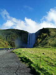Sk&oacute;gafoss waterfall at the mountains with a river water flowing the grass green nature down to hike and walk tourist up and drive in iceland