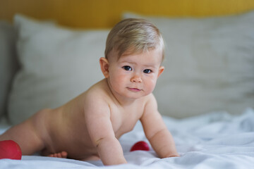 super sweet naked almost one year old happy blond baby boy lying at home on a cozy bed after...