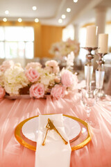 table decoration with pink tablecloth, crystal candlesticks with candles and white pink flowers in restaurant . stylish wedding day. setting table with gold plate, fork and knife