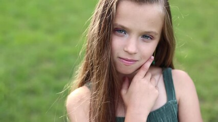 front view of adorable little girl with hairstyle is smiling with her outdoors on summer day. caucasian friendly and shy kid looking at camera posing. Happy childhood on holiday vacation.