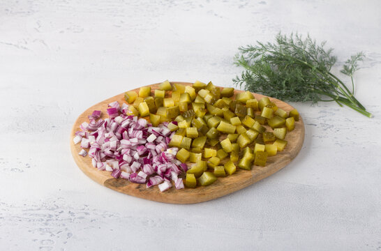 Wooden board with chopped red onion, pickles and a bunch of dill on a light blue background. Cooking homemade food