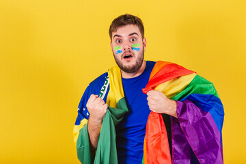Brazilian caucasian man, soccer fan from Brazil, holding LGBT flag, concept of gender equality,...