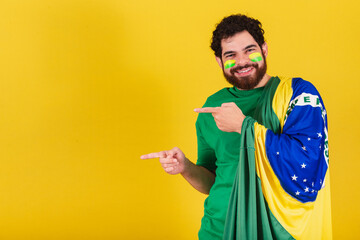 caucasian man with beard, brazilian, soccer fan from brazil, pointing left with finger, photo for advertisement, indication.