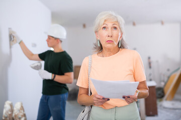 Portrait of anxious senior woman holding work contract for teenage boy who working in as plasterer...