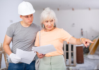 Portrait of mature woman architect talking with teenager construction worker in apartment under reconstruction, examining documents and planning work process for renovation