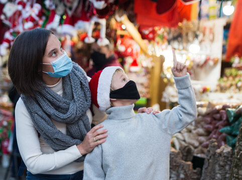 Happy Tween Boy With His Mother In Protective Masks To Prevent Spread Of Viral Infections Choosing Xmas Decorations And Gifts On Street Fair ..