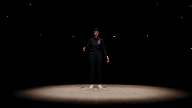 talented dancer woman is standing alone on scene in bright soffit light, popping dance style