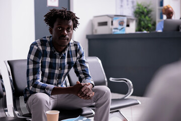 Portrait of male patient sitting in waiting room, having checkup examination appointment with...