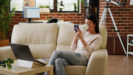 Happy woman sending messages on mobile phone while doing work from home and listening to music. Joyful person texting coworker on touchscreen phone while working remotely. Handheld shot