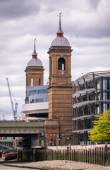 Naklejka premium London, England, UK - July 6, 2022: From Thames River. 2 Brown stone gate towers with spires on north shore at Cannon Street Railway bridge under white cloudscape.