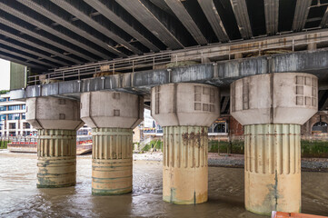 London, England, UK - July 6, 2022: From Thames River. Thck concrete support columns or piles of Cannon Street Railway bridge standing in river.