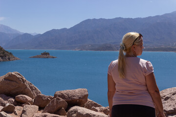 Blonde woman looking a beautiful scenery with a lake and mountains on a sunny day.
