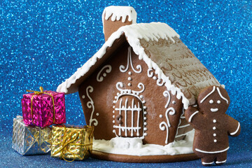 Gingerbread house, gifts in colorful boxes and a gingerbread man on a sparkling blue background. An...