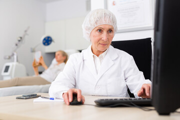 Portrait of professional experienced female cosmetologist working with laptop in modern aesthetic medicine office, writing patient examination results