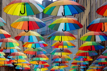 Fototapeta na wymiar Colorful rainbow umbrella between building above pink street, Small road in city center of Lisbon, Symbol of Gay, Lesbian, Bisexual and Transgender, LGBT community and social movements, Portugal.
