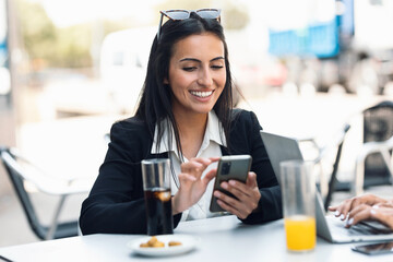 Beautiful stylish woman sending messages with smartphone while having breakfast sitting in the eco bar terrace.