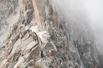 A mountaineer walks, seen from afar, along the spiers of a mountain.