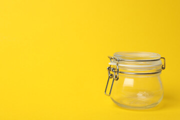 Closed empty glass jar on yellow background, space for text