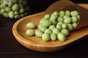 Tasty wasabi coated peanuts on wooden table, closeup