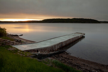Stone covered jetty by beach and calm water in sunrise ligth at a fjord in southern Norway