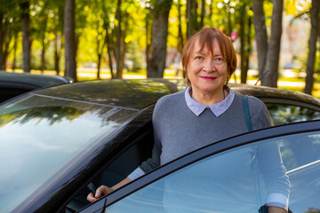 Positive mature woman standing beside her car and smiling.