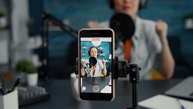 Modern smartphone recording vlogger talking to public while sitting at home studio desk. Famous influencer filming podcast show with touchscreen display device while sitting in living room. Close up