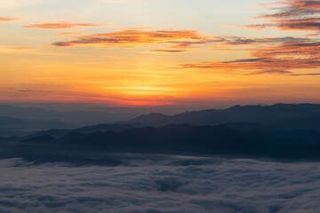 Aerial view of vibrant sunset over white dense clouds with distant dark mountains on horizon.