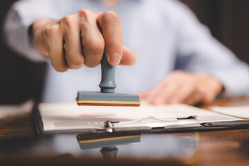 Fototapeta premium Close-up of a person's hand stamping with approved stamp on certificate document public paper at desk, notary or business people work from home, isolated for coronavirus COVID-19 protection