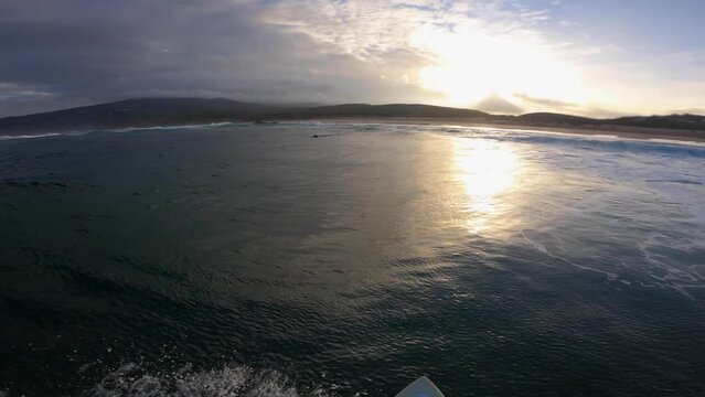 Sun sets over ocean surface, underwater POV with some clouds and surfing at same time.