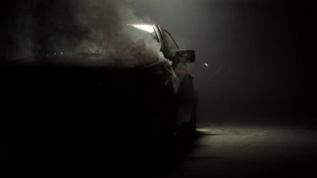 Smoke comes from under the hood of a red car on set. Dark atmospheric shot.