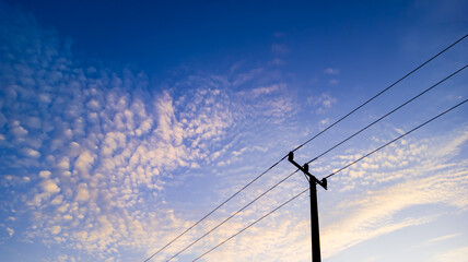 Power pole silhouette with white cloud texture in blue sky at sunrise, minimalist black electric pole on blue sky background at sunrise