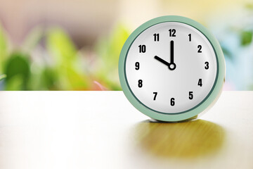 Alarm clock on brown wood desk and  blurred greenery background with copy space.