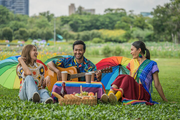 LGBTQ people friends enjoying picnic together and playing guitar in park