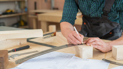 A carpenter measures wooden planks and makes marks with a pencil in a workshop.