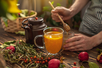 Woman is making a tasty and healthy vitamin tea from fresh sea buckthorn berries with honey. Concept of a cozy autumn atmosphere and health care during colds and flu season