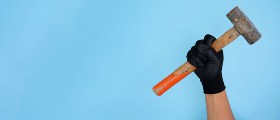 Hand wearing black gloves holding wooden sledge hammer isolated baby blue background with copy space