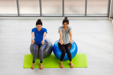 Above two Asian adult and young woman in sportswear doing aerobics yoga exercise with sitting on fitness ball indoor yoga studio, fit sport healthy workout lifestyle exercise