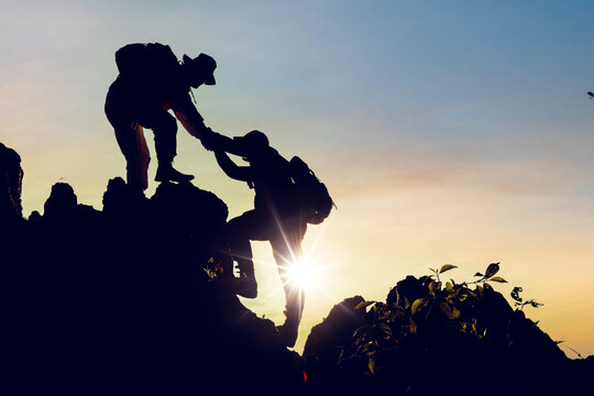 Silhouette climbing buddies help each other climb up the mountain at sunrise as the right lifestyle idea