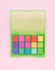 A large set of multi-colored eyeshadow on a pink background. Flat lay.
