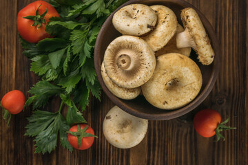 A bowl with large wild mushrooms, vegetables and celery leaves on a wooden table. Flat lay.
