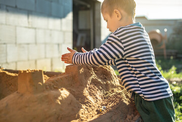 Little boy is playing outside near the house and building a sand castle