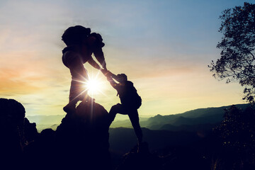 Silhouette climbing buddies help each other climb up the mountain at sunrise as the right lifestyle...