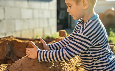 Little boy is playing outside near the house and building a sand castle