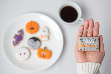 woman hand holding funny Halloween Cookie during drinking coffee. Happy Halloween day, Trick or Threat, Hello October, fall autumn, Traditional, party and holiday concept