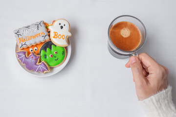 woman hand holding coffee cup during eating funny Halloween Cookies. Happy Halloween day, Trick or Threat, Hello October, fall autumn, Traditional, party and holiday concept