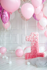 pink helium balloons and number one, on background of white wall and wooden floor. Greeting or...