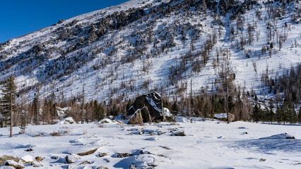 Picturesque boulders in the valley are covered with a layer of snow. The forest grows on a mountain...