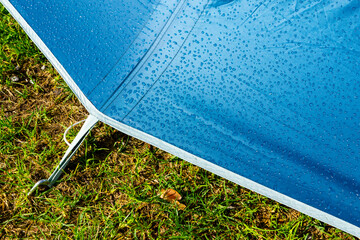 sparkling in the sunlit early morning dew on the surface of waterproof blue fabric of a tourist...